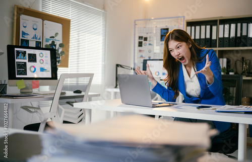 Businesswoman is experiencing extreme stress while working at her desk, surrounded by paperwork and digital devices. She appears overwhelmed and frustrated