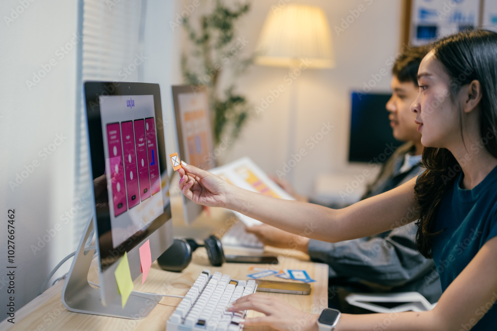 Two web designers are working together on the user experience for a mobile application using sticky notes to rearrange elements on the screen Two web designers are working together on the user experience for a mobile application using sticky notes to rearrange elements on the screen