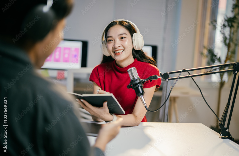 In a cozy studio, a podcaster conducts an engaging interview with a young asian woman, both immersed in creating captivating audio content In a cozy studio, a podcaster conducts an engaging interview with a young asian woman, both immersed in creating captivating audio content