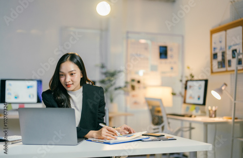 Canvas Print Focused young asian businesswoman in modern office working diligently at desk wi