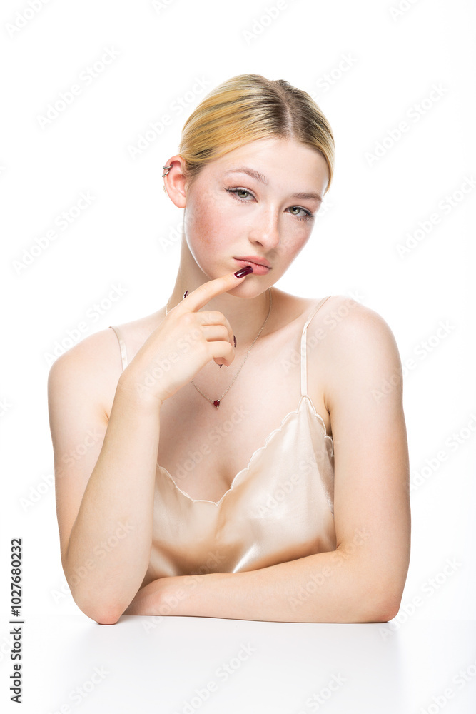 Fototapeta premium A young blonde girl with freckles in a golden top. Beauty portrait of a woman on a white background in the studio.