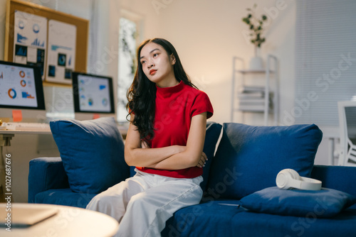 Young woman is sitting on a blue sofa with her arms crossed, feeling stressed out. She is working from her home office