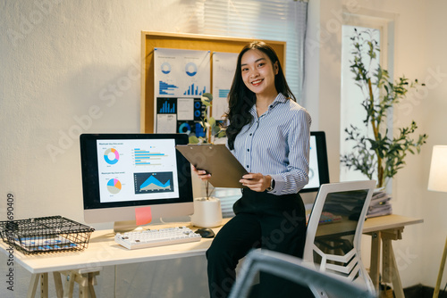 Confident asian businesswoman in modern office, smiling with clipboard and charts, focused on growth and success