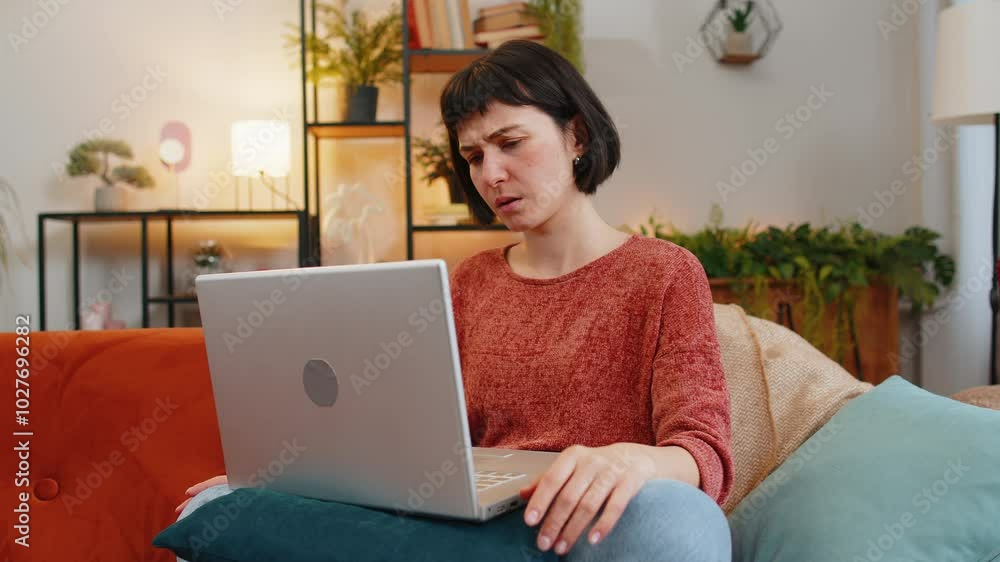 Angry woman using laptop typing browsing working, loses becoming surprised sudden lottery results bad news fortune loss fail computer virus. Upset Caucasian girl on couch in living room at home. Angry woman using laptop typing browsing working, loses becoming surprised sudden lottery results bad news fortune loss fail computer virus. Upset Caucasian girl on couch in living room at home.
