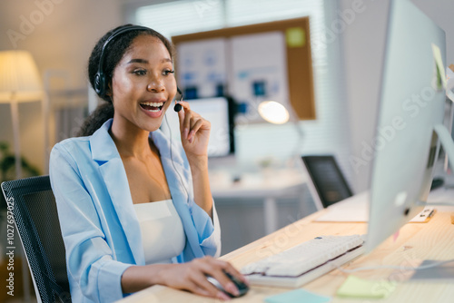 African american businesswoman is smiling while talking on a headset and working on her computer at her bright and modern office