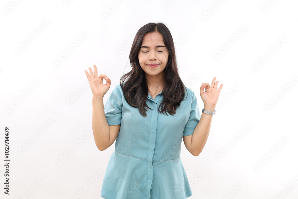 Calm relieved young Asian woman shows zen or okay sign meditates in good mood stands with eyes closed isolated on white background Calm relieved young Asian woman shows zen or okay sign meditates in good mood stands with eyes closed isolated on white background