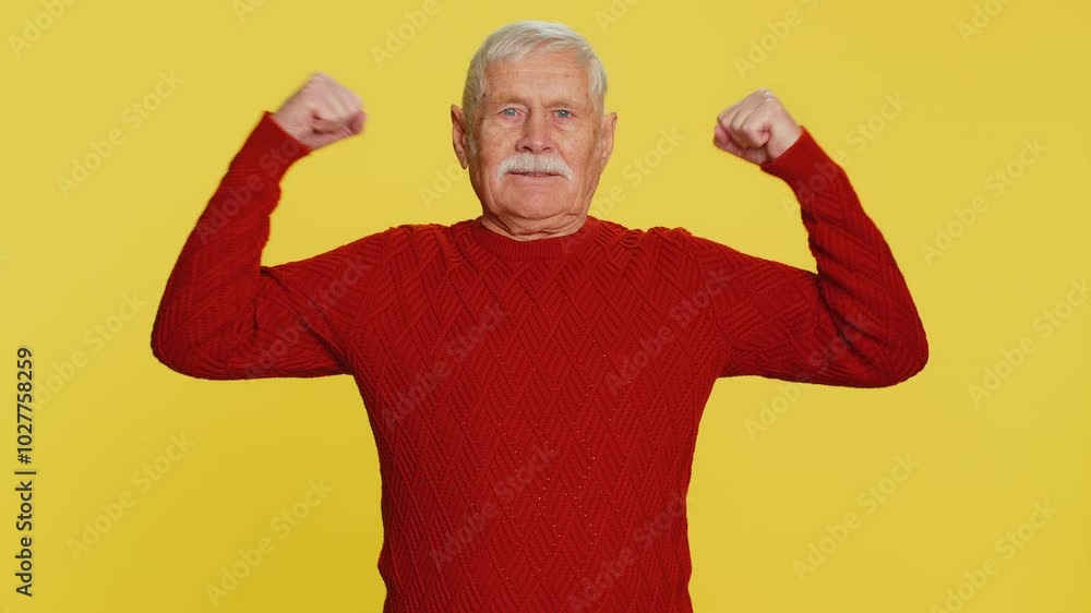 I am strong and independent. Old senior man showing biceps and looking confident, feeling power strength to fight for rights, energy to gain success win. Grandfather isolated on yellow background