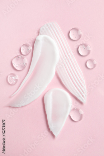 Smears of different cosmetic products on pink background, top view