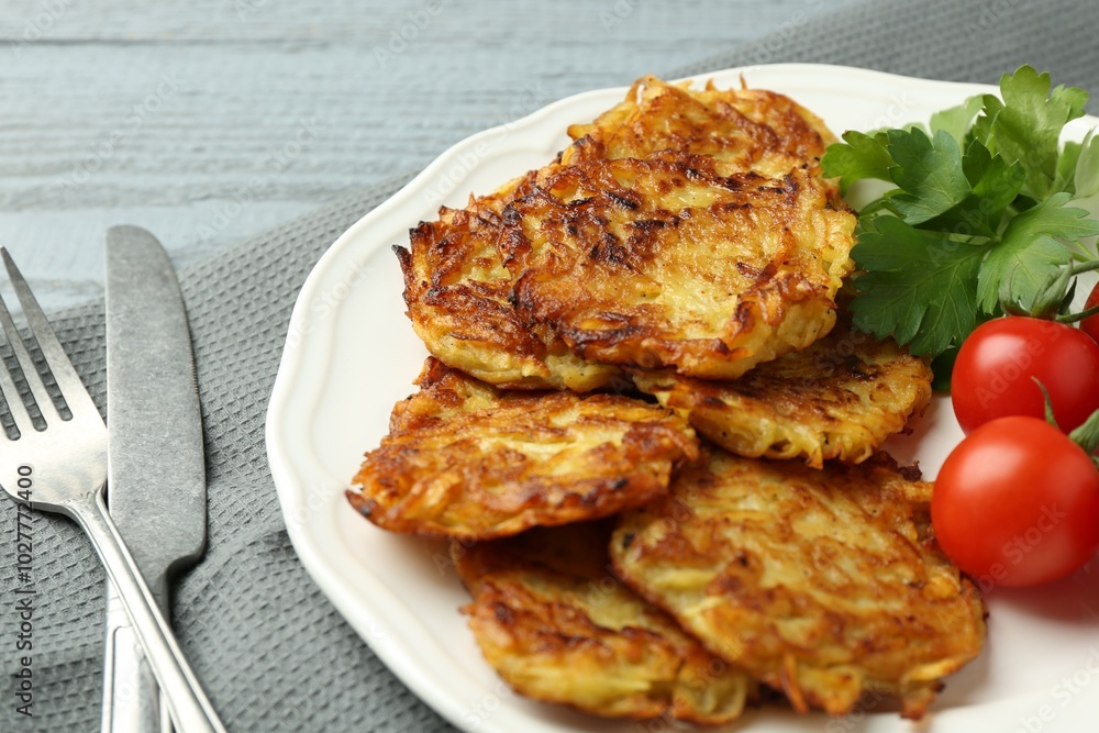 Delicious potato pancakes with tomatoes and parsley served on gray wooden table, closeup Delicious potato pancakes with tomatoes and parsley served on gray wooden table, closeup