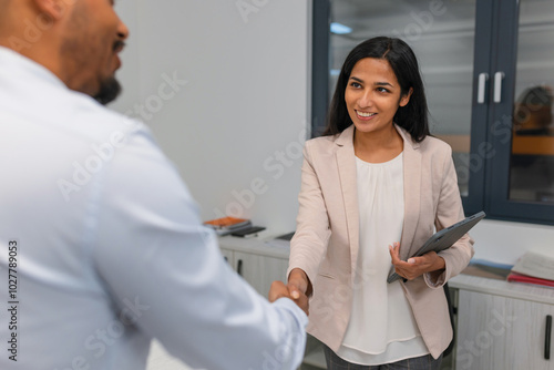 Indian female hiring manager shaking hands with an African American male candidate at the end of a successful job interview.