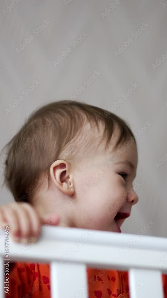Cheerful happy baby boy standing in the cot waving hand with pacifier
