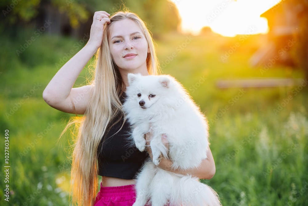 Young lady stands in a field at sunset, holding her white fluffy dog Young lady stands in a field at sunset, holding her white fluffy dog