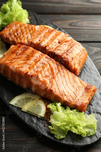 Delicious grilled salmon fillets with lettuce and lemon on wooden table, closeup