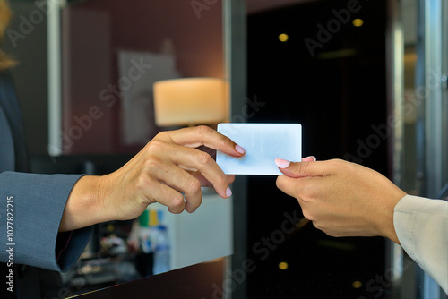 Close-up of hotel keycard exchange between two people at reception desk.
