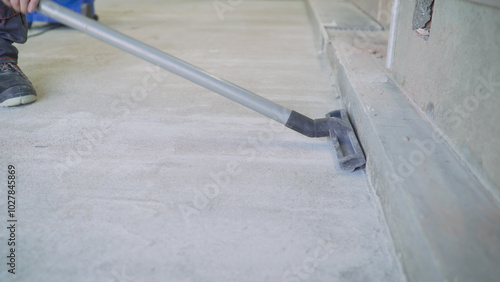 Construction worker vacuuming dust on concrete floor.