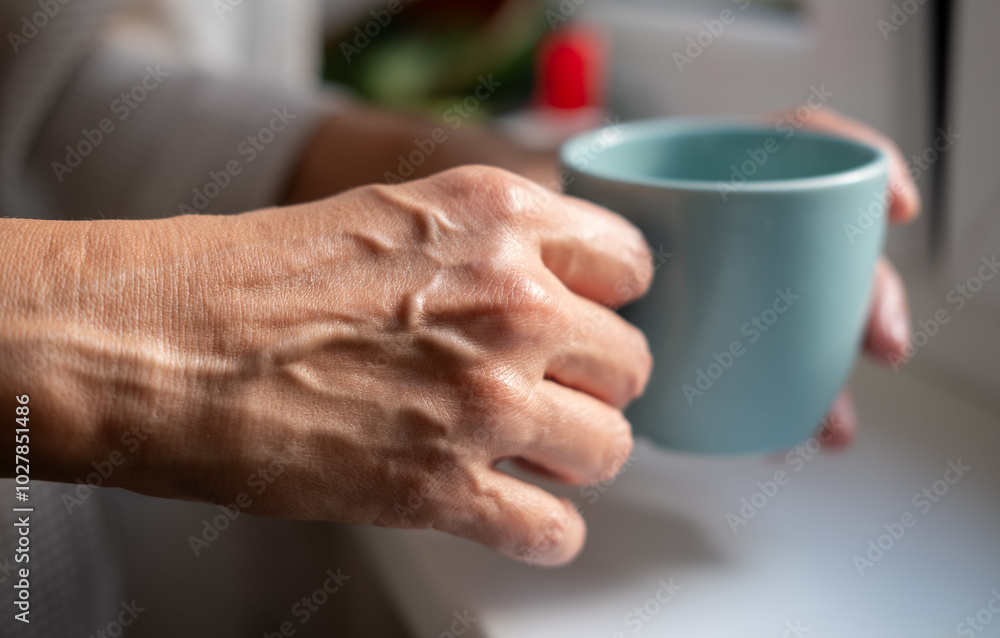 Mature woman hands is holding tea or coffee cup near window at home. Concept of domestic lifestyle. Cropped photo of modern happy middle aged lady wearing bathrobe at sunny day Mature woman hands is holding tea or coffee cup near window at home. Concept of domestic lifestyle. Cropped photo of modern happy middle aged lady wearing bathrobe at sunny day