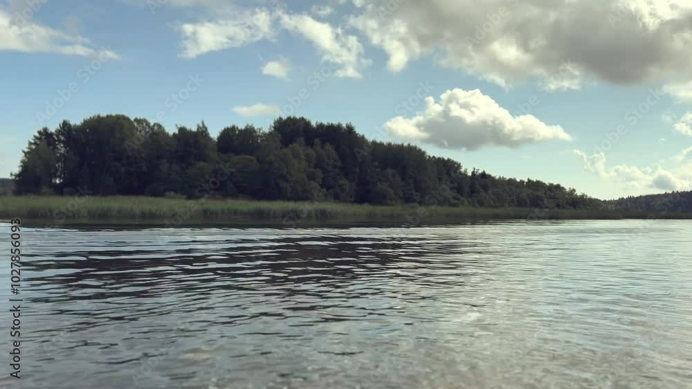 The video shows fast movement along a river, with lush green forest on the bank and reeds lining the waters edge. The rapid pace creates a dynamic view of the natural landscape and shoreline. High The video shows fast movement along a river, with lush green forest on the bank and reeds lining the waters edge. The rapid pace creates a dynamic view of the natural landscape and shoreline. High