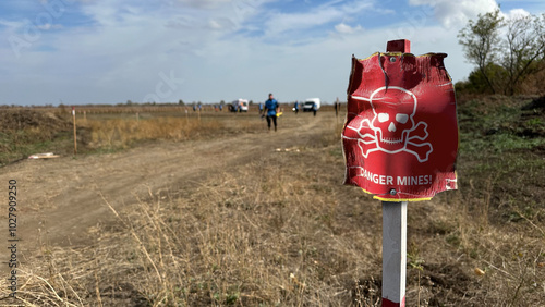 Photos danger sign mine in Ukrainian near an agricultural field during war in Ukraine, with people from demining team in background