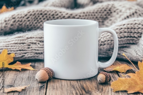 A cozy, empty white mug surrounded by autumn leaves and acorns on a rustic wooden table draped with a soft knitted blanket in fall