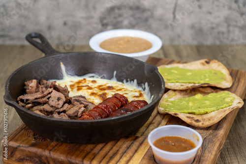 Grilled carne asada meat sliced into bite size pieces in a cast iron skillet served with chorizo sausage, guacamole, and beans on a wooden platter