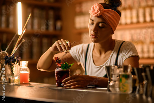 Female bartender decorates a glass with a black drink with orange chips photo