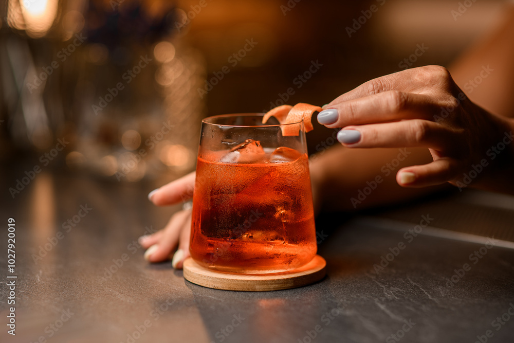 Female hands decorate a glass with a drink and ice with a piece of peel Female hands decorate a glass with a drink and ice with a piece of peel