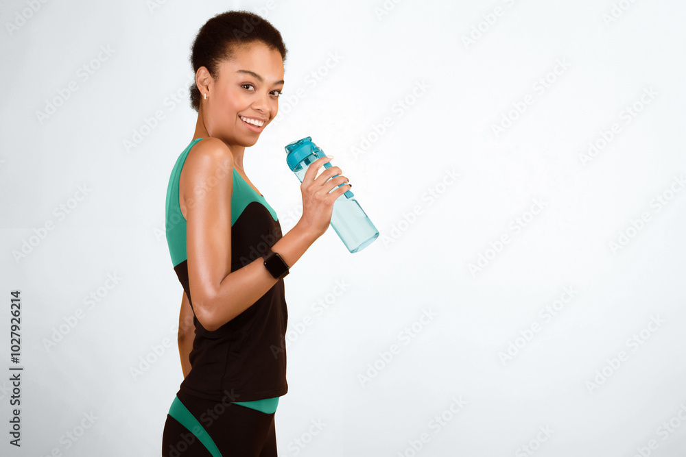 Happy Afro Girl In Fitwear Holding Bottle Of Water Posing Over Yellow Studio Background. Workout And Hydration. Copy Space