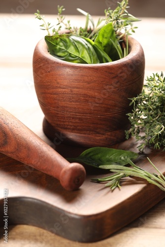 Different fresh herbs in mortar with pestle on wooden table