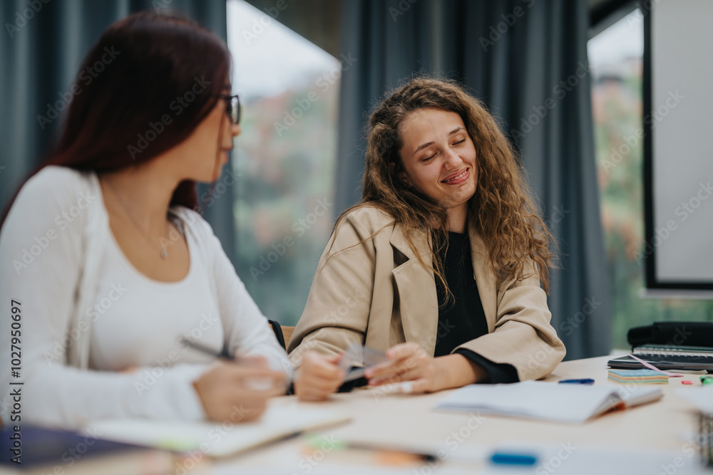 Two female students sitting at a table, discussing classwork and exchanging ideas in a classroom setting. They appear focused and enjoy collaborative learning experience, highlighting educational Two female students sitting at a table, discussing classwork and exchanging ideas in a classroom setting. They appear focused and enjoy collaborative learning experience, highlighting educational