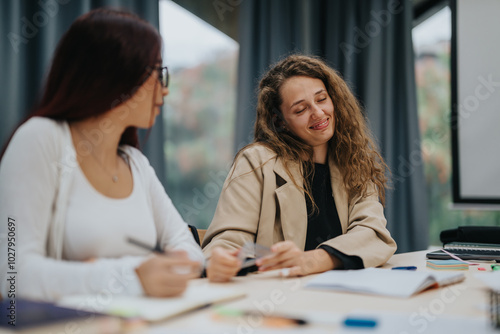 Two female students sitting at a table, discussing classwork and exchanging ideas in a classroom setting. They appear focused and enjoy collaborative learning experience, highlighting educational