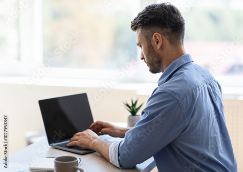 Busy Male Entrepreneur Working On Laptop With Black Blank Screen In Office, Typing On Keyboard, Over Shoulder View, Mockup