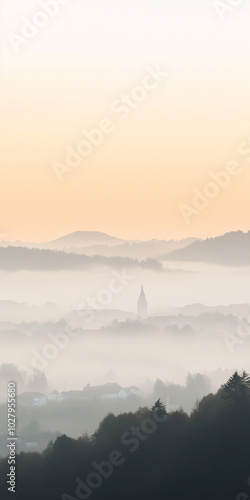 Silhouette of hills, forests, and a city enveloped in fog during sunset, creating a serene and atmospheric landscape perfect for mobile phone wallpapers