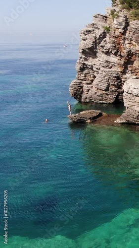 Aerial view of vacationers making exercises on the rock shore of blue sea 