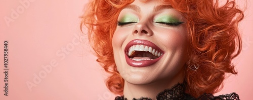 Vibrant drag queen with orange hair and bright makeup laughing joyfully against a pink background