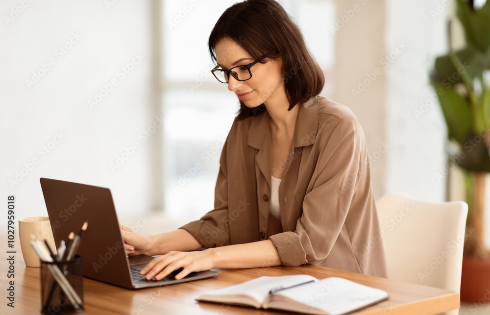 Making New Project. Portrait of satisfied girl in eyeglasses using laptop, working at home, writing blog, free space Making New Project. Portrait of satisfied girl in eyeglasses using laptop, working at home, writing blog, free space
