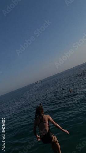 Brave young girl jumping off a cliff into the clear sea.