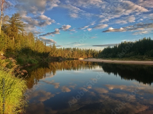 The river in the forest reflects the blue sky with clouds. Silence