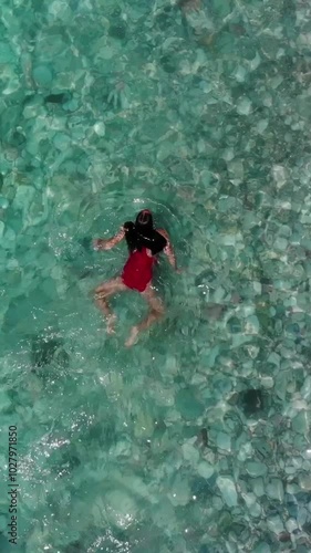 Girl in a red swimsuit swimming in a transparent green blue lagoon on a bright sunny day.