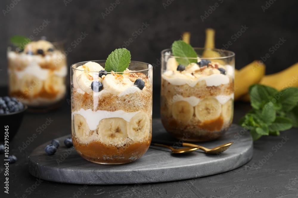 Tasty trifle dessert. Sponge cake, blueberries, banana and whipped cream in glasses on black table Tasty trifle dessert. Sponge cake, blueberries, banana and whipped cream in glasses on black table