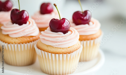 delicious cupcakes topped with pink frosting and cherries. The cupcakes are arranged on a white plate, showcasing their soft texture and appealing colors.