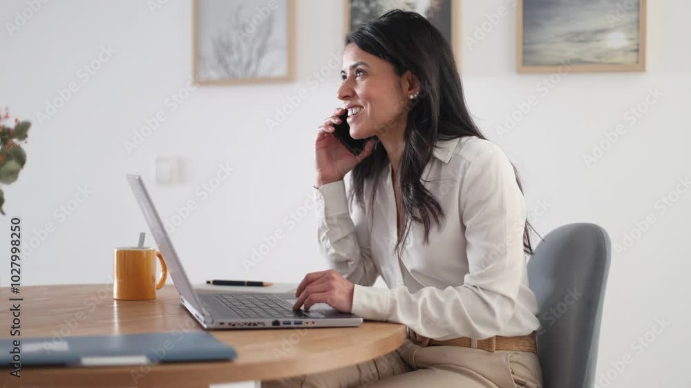 Businesswoman is multitasking while working from home, talking on her phone and working on her laptop Businesswoman is multitasking while working from home, talking on her phone and working on her laptop