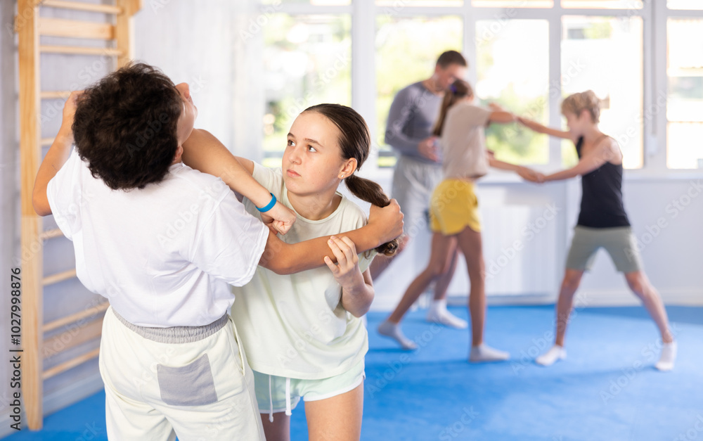 Fototapeta premium Boy and girl training self-defense techniques in group in studio