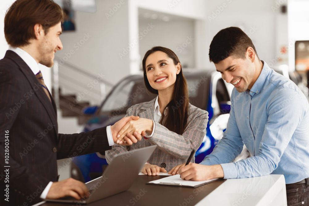 Young Spouses Buying Car, Beautiful Wife Handshaking With Seller Man Standing In Dealership Office. Selective Focus Young Spouses Buying Car, Beautiful Wife Handshaking With Seller Man Standing In Dealership Office. Selective Focus