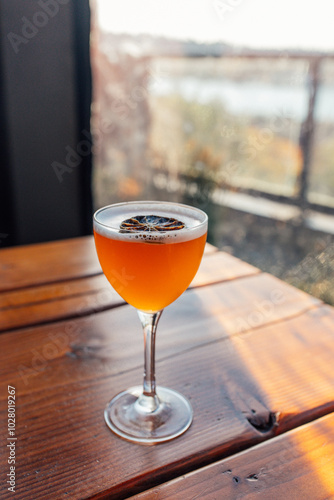 orange cocktail with foam and dehydrated lime in nick and nora glass on outdoor table 