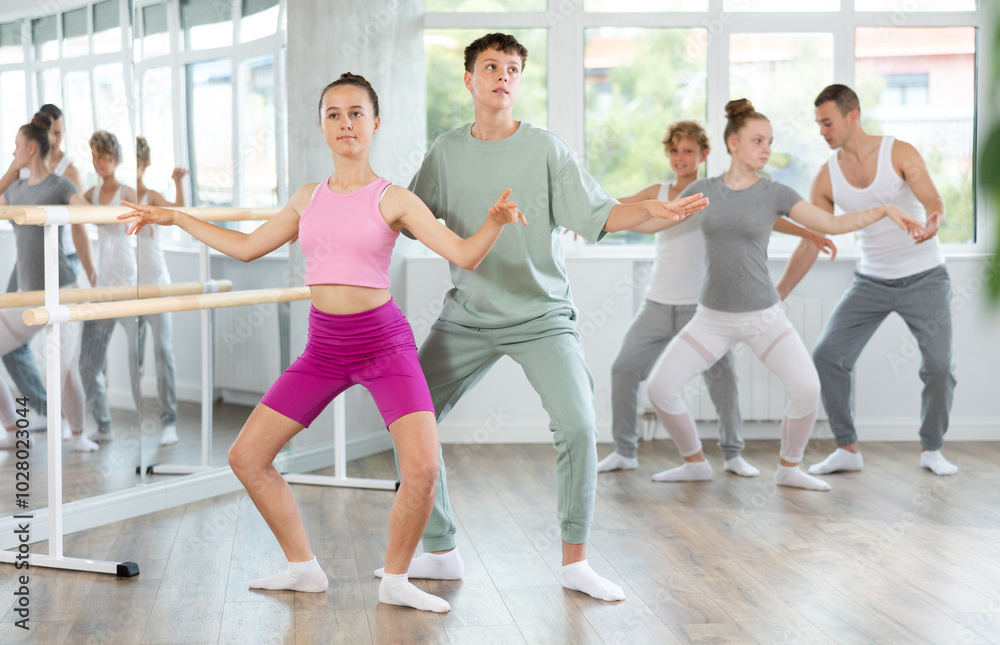 Fototapeta premium Slim teen boy and girl doing together plie position of ballet during choreography classes