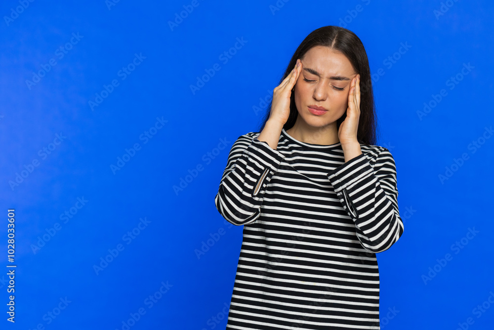 Attractive exhausted young woman girl rubbing temples to cure headache problem, suffering from tension, migraine stress, grimacing in pain, high blood pressure isolated alone on blue wall background Attractive exhausted young woman girl rubbing temples to cure headache problem, suffering from tension, migraine stress, grimacing in pain, high blood pressure isolated alone on blue wall background