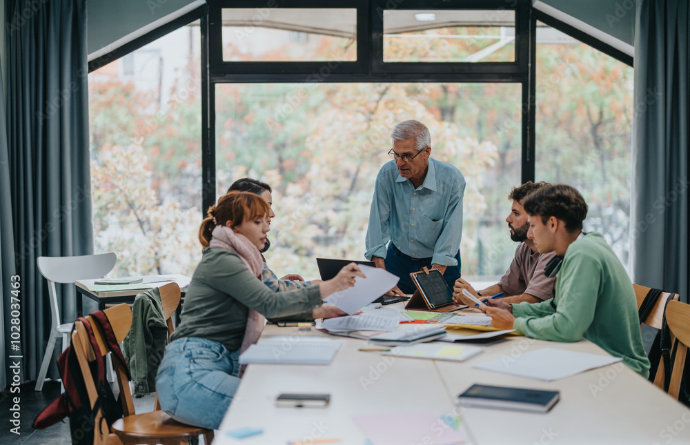 A group of university students working together on a project, receiving guidance from a senior professor in a classroom setting. A group of university students working together on a project, receiving guidance from a senior professor in a classroom setting.