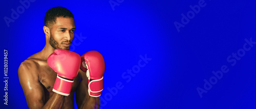 Boxing Sport. Shirtless Professional Boxer Standing In Ready-To-Fight Position, Wearing Gloves On Blue Background. Studio Shot, Copy Space