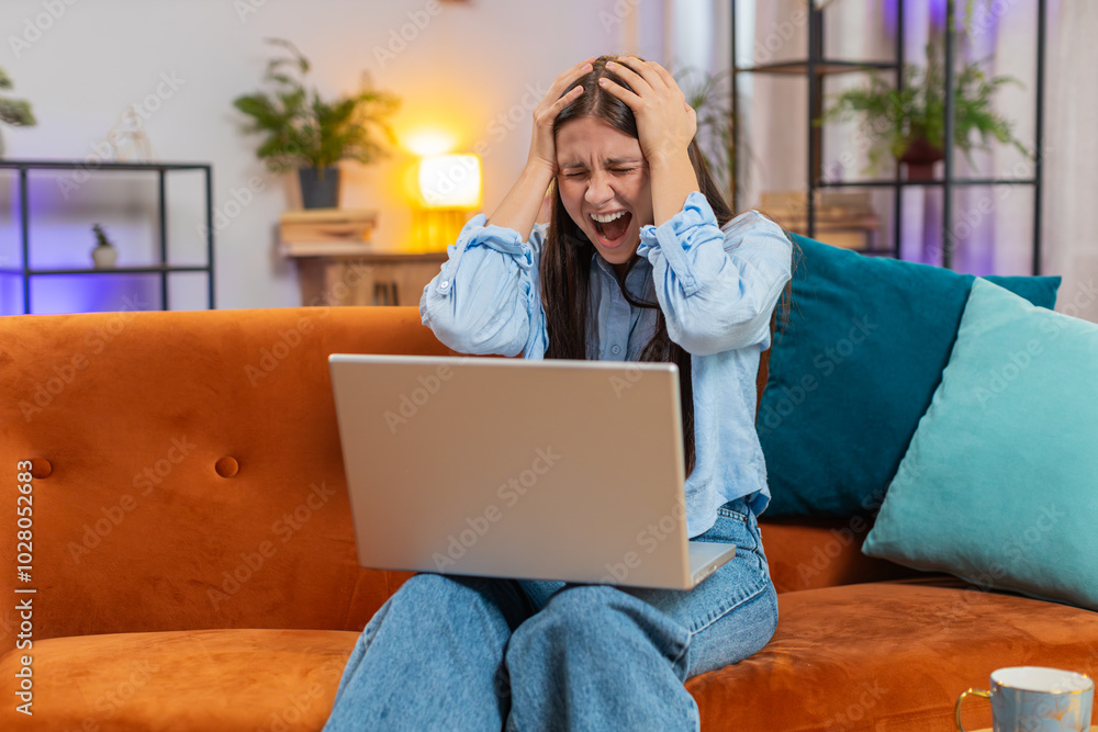 Fototapeta premium Upset woman sitting on sofa at home using laptop having anxiety stress, searching internet can't find information. Shocked girl reacting to loss bad news on netbook in room apartment. Computer virus