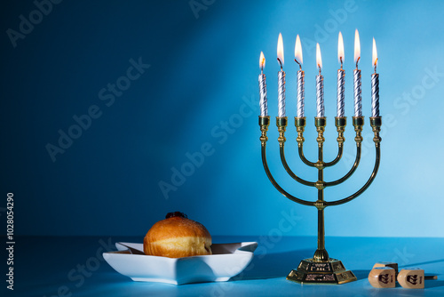 Jewish holiday Hanukkah concept. Menorah with burning candles, jelly donut, dreidels on blue background.